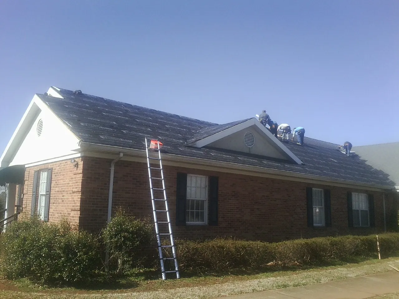 Crew tearing shingles off a brick ranch roof with a ladder set — Emergency Roof Repair work by our crew in Feeding Hills