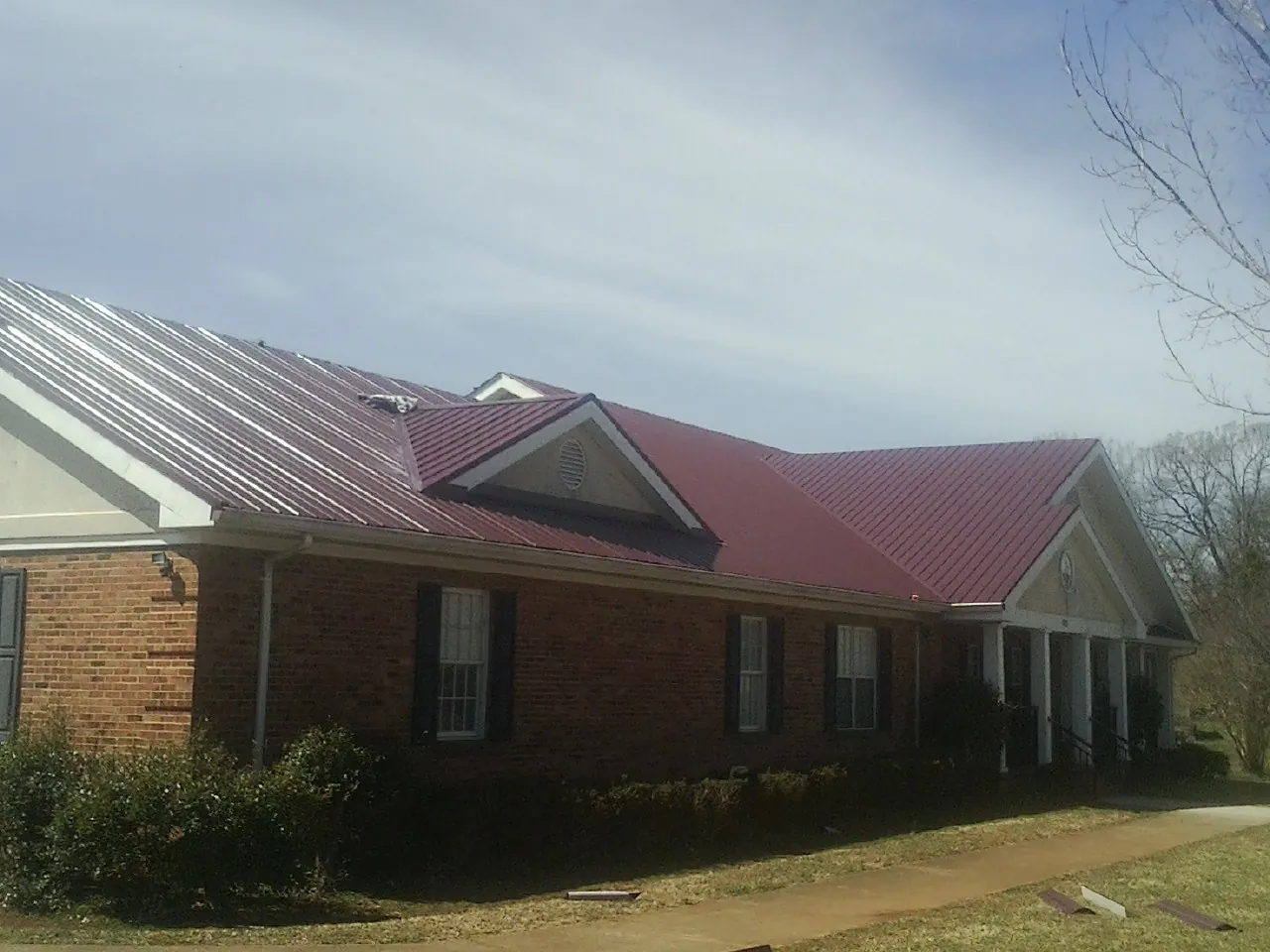 Red metal roof with gabled entries on a long brick building, from a Hail Damage Roof Repair job in Feeding Hills