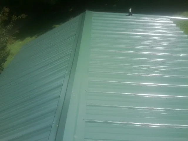 New green metal panels meeting at the ridge of a roof — Flat Roof Repair work by our crew in Feeding Hills