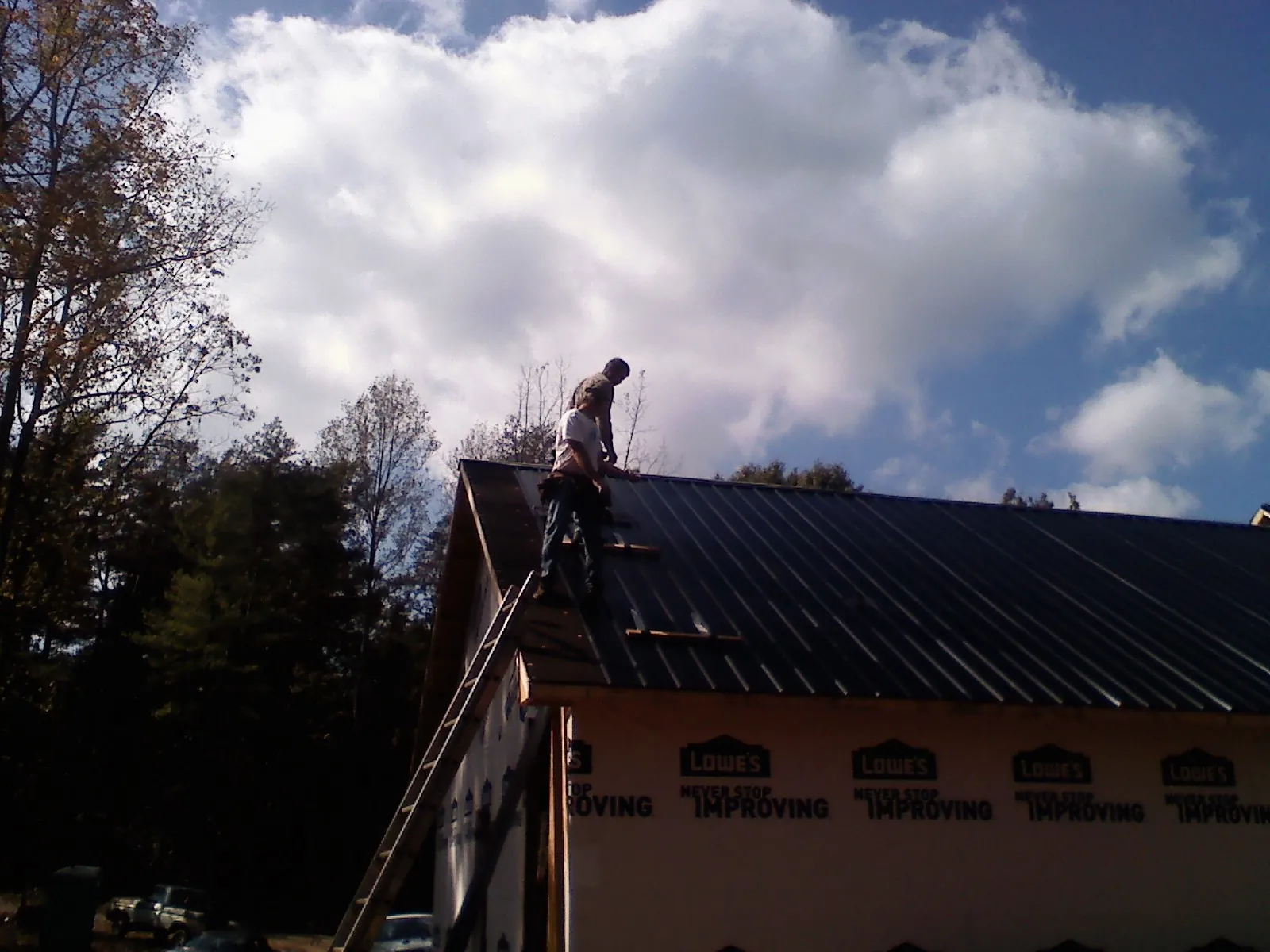Roofer fastening dark metal panels high against a cloudy sky, from a Roof Inspection job in Feeding Hills