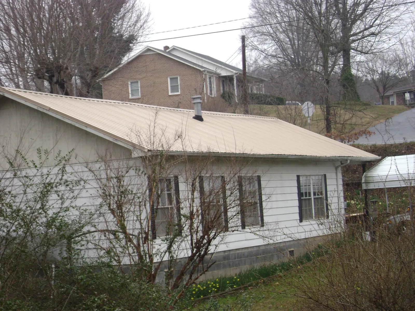 Tan metal roof on a white sided house set into a hillside — Commercial Roofing by Roofing Brothers in Feeding Hills