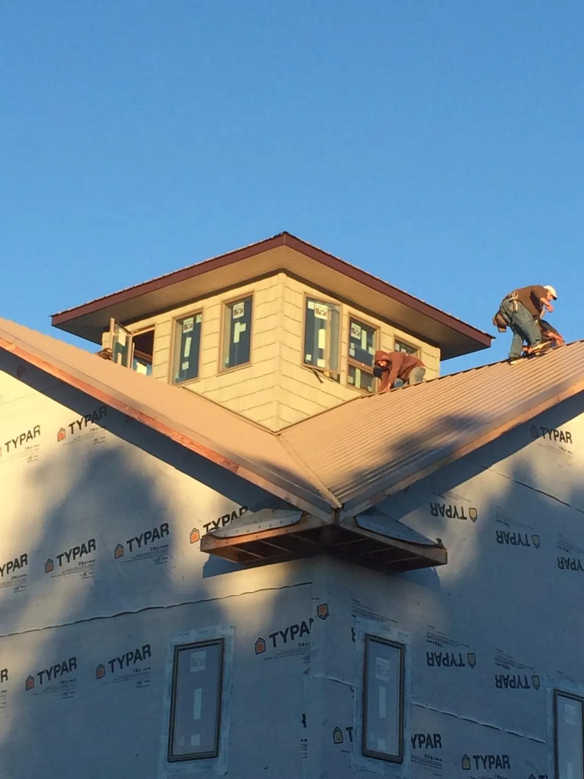 Roofers working around a rooftop cupola on a new metal roof at sunset — Roof Waterproofing in Feeding Hills by Roofing Brothers